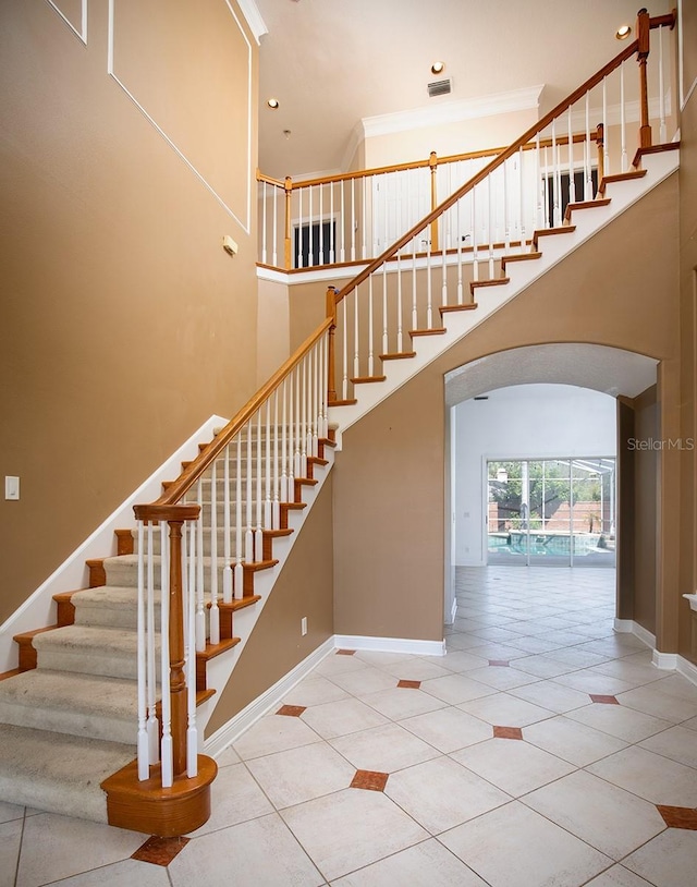 staircase featuring arched walkways, tile patterned flooring, a towering ceiling, and baseboards