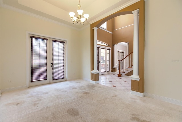 foyer featuring light carpet, arched walkways, a tray ceiling, french doors, and ornate columns