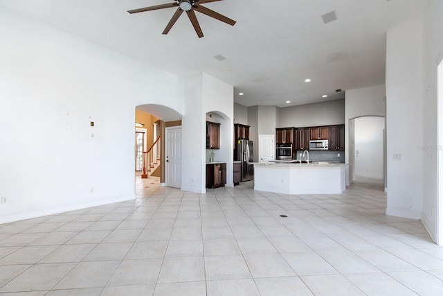 unfurnished living room with a towering ceiling, light tile patterned floors, arched walkways, and a ceiling fan