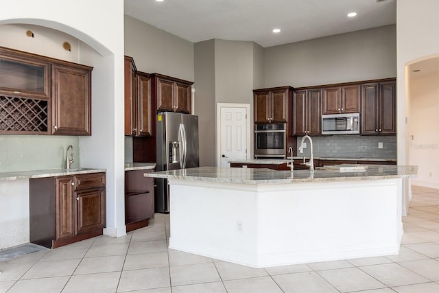 kitchen with stainless steel appliances, light stone counters, a sink, and a center island with sink