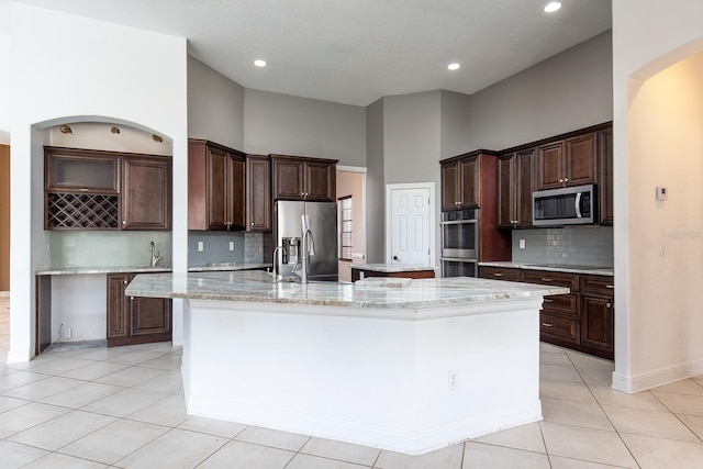 kitchen featuring light tile patterned floors, stainless steel appliances, a spacious island, a high ceiling, and dark brown cabinetry