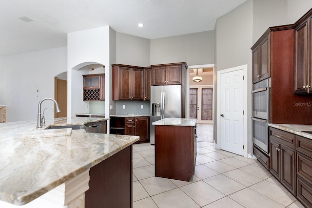 kitchen with light tile patterned floors, a center island, a high ceiling, stainless steel appliances, and a sink