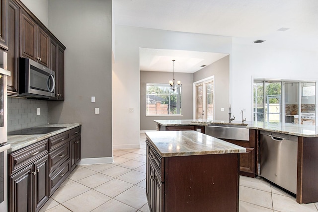 kitchen with light tile patterned floors, a sink, a kitchen island, appliances with stainless steel finishes, and backsplash