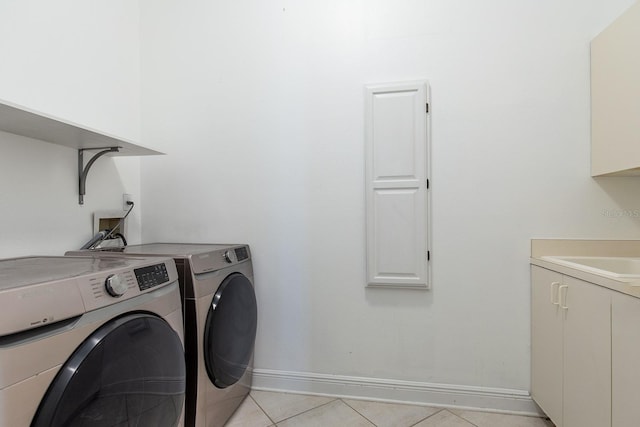 laundry area featuring light tile patterned floors, cabinet space, baseboards, washing machine and clothes dryer, and a sink