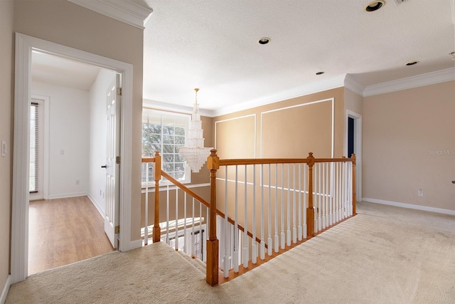 hallway featuring a chandelier, an upstairs landing, baseboards, carpet, and crown molding