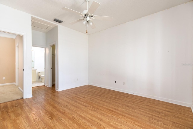 empty room with visible vents, light wood-style flooring, a ceiling fan, attic access, and baseboards