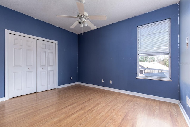 unfurnished bedroom with a closet, light wood-style floors, ceiling fan, a textured ceiling, and baseboards