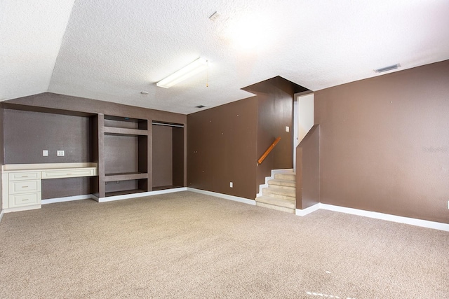 interior space with visible vents, stairs, a textured ceiling, carpet floors, and built in desk