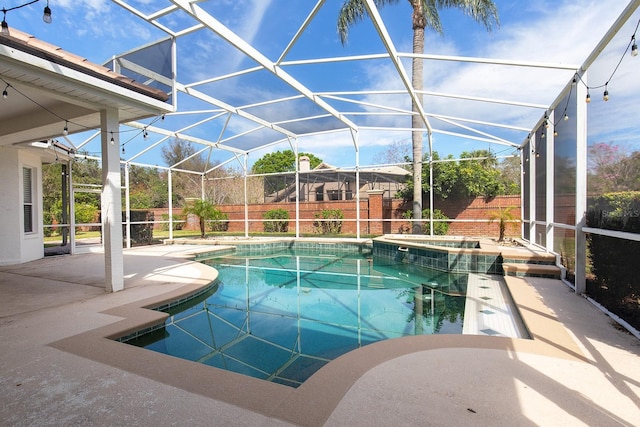 view of swimming pool with a patio, a pool with connected hot tub, fence, and glass enclosure