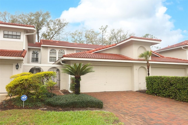 mediterranean / spanish house with a garage, decorative driveway, a tile roof, and stucco siding