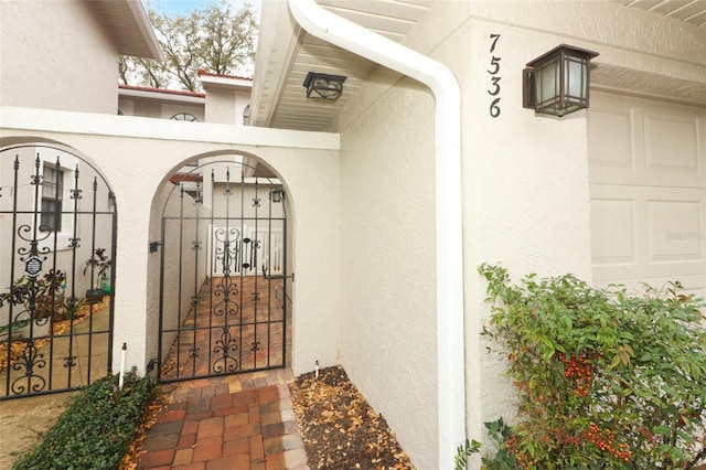 property entrance featuring a gate, fence, and stucco siding