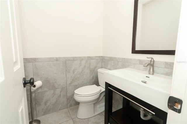 half bath with toilet, vanity, tile walls, and tile patterned floors