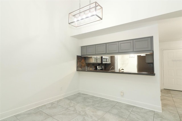 kitchen with baseboards, dark countertops, stainless steel microwave, gray cabinets, and backsplash