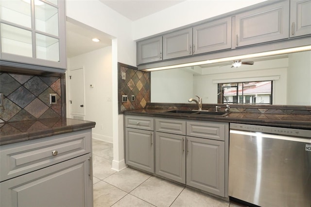 kitchen featuring stainless steel dishwasher, dark countertops, a sink, and gray cabinetry