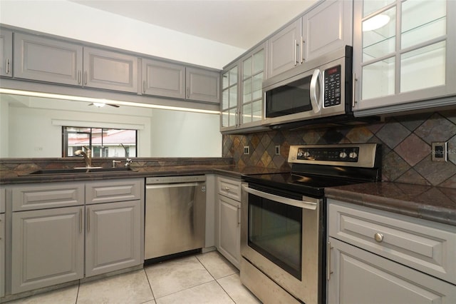 kitchen featuring light tile patterned floors, decorative backsplash, gray cabinetry, appliances with stainless steel finishes, and a sink