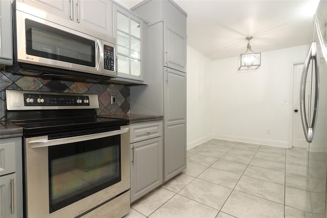 kitchen featuring light tile patterned floors, stainless steel appliances, dark countertops, backsplash, and baseboards