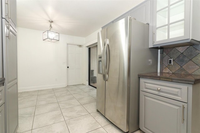 kitchen with light tile patterned floors, stainless steel fridge, baseboards, dark countertops, and backsplash