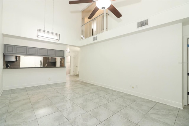 unfurnished living room featuring a ceiling fan, a towering ceiling, visible vents, and baseboards