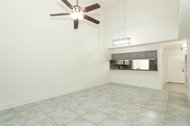 unfurnished living room featuring a towering ceiling, ceiling fan, and baseboards