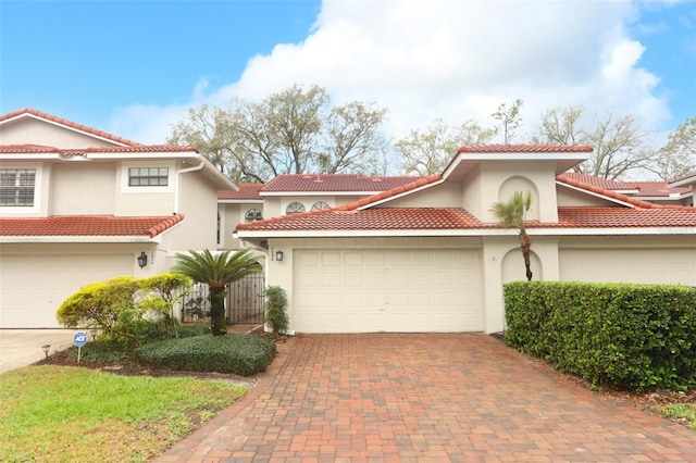 mediterranean / spanish-style home featuring decorative driveway, stucco siding, an attached garage, fence, and a tiled roof