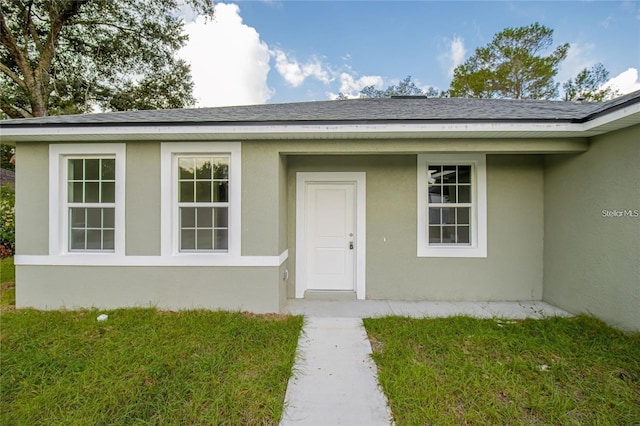 doorway to property with stucco siding, a shingled roof, and a yard