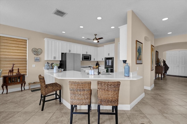 kitchen with arched walkways, stainless steel appliances, light countertops, a peninsula, and a kitchen breakfast bar