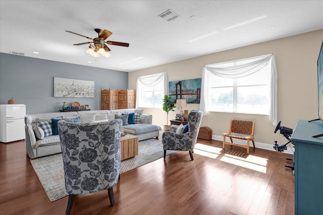 living area featuring a ceiling fan, wood finished floors, visible vents, and baseboards