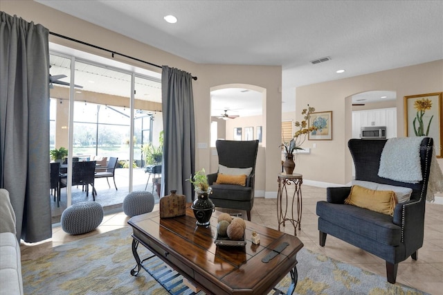 living area featuring arched walkways, light tile patterned flooring, visible vents, and baseboards