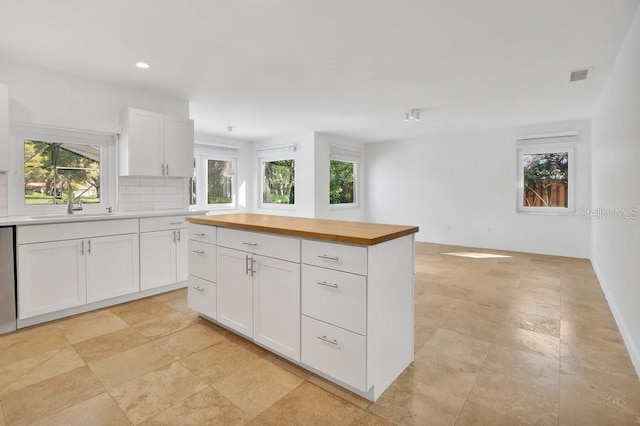 kitchen with visible vents, decorative backsplash, white cabinets, a sink, and butcher block countertops