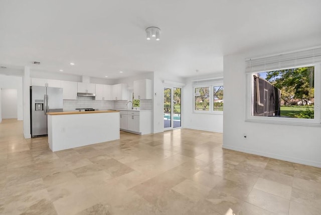 kitchen with under cabinet range hood, a kitchen island, white cabinetry, stainless steel refrigerator with ice dispenser, and tasteful backsplash