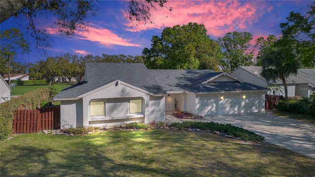 ranch-style home with a garage, fence, concrete driveway, stucco siding, and a front yard