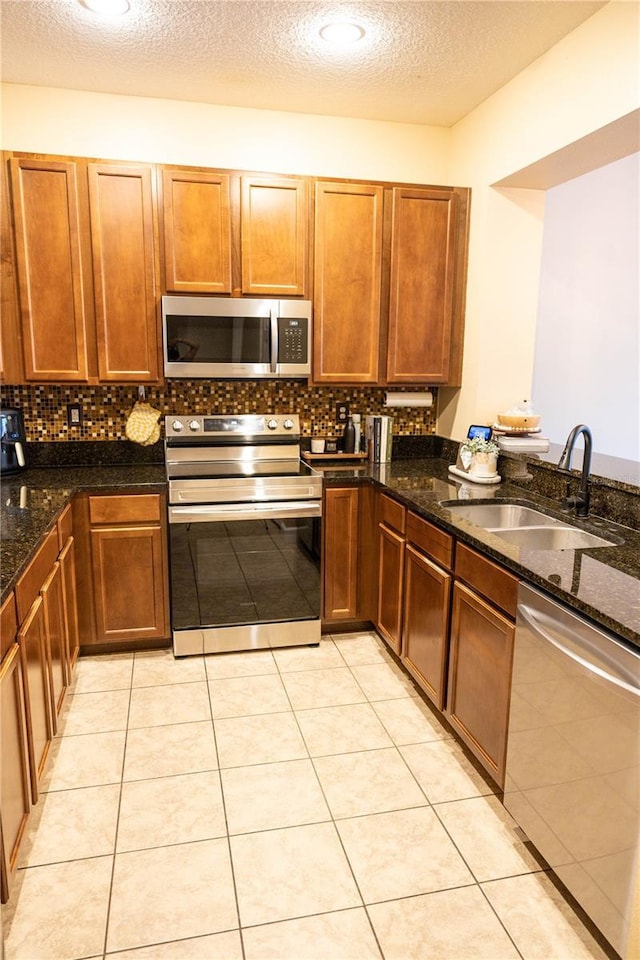 kitchen featuring a sink, stainless steel appliances, tasteful backsplash, and dark stone countertops