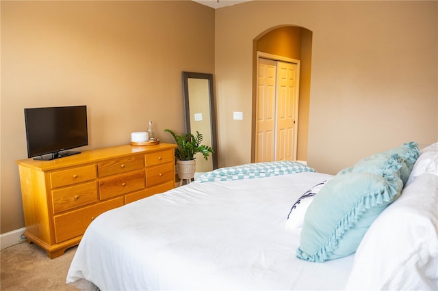 bedroom featuring a closet, arched walkways, light colored carpet, and baseboards