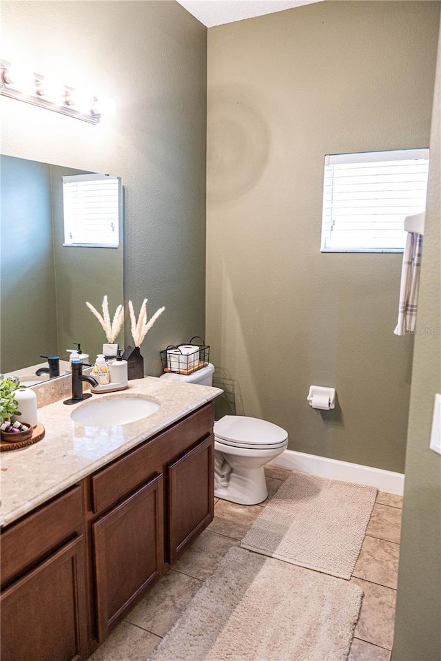 half bathroom featuring plenty of natural light, toilet, vanity, and baseboards