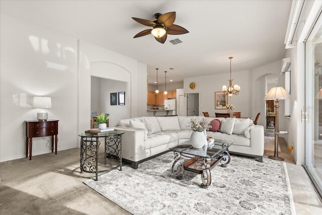 living room with arched walkways, light colored carpet, ceiling fan with notable chandelier, visible vents, and baseboards