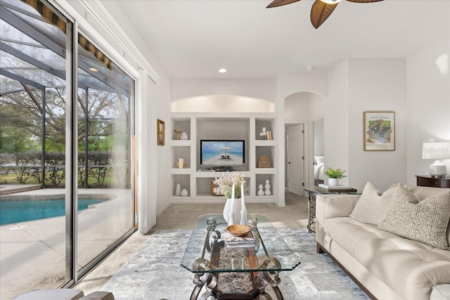 living area with built in shelves, arched walkways, a ceiling fan, and recessed lighting