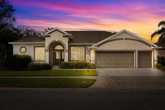 ranch-style home with an attached garage, driveway, roof with shingles, stucco siding, and a front yard