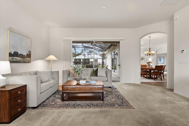 carpeted living area featuring arched walkways, visible vents, and an inviting chandelier