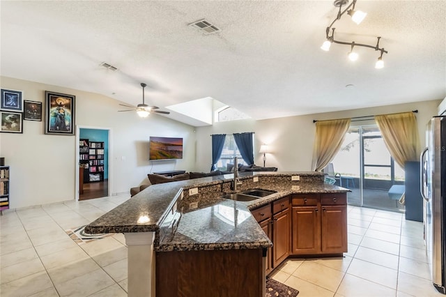 kitchen featuring lofted ceiling, a sink, visible vents, open floor plan, and freestanding refrigerator