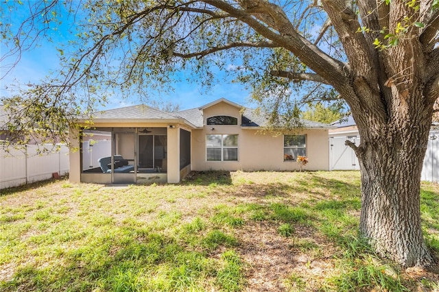 rear view of house featuring stucco siding, a lawn, a gate, a sunroom, and a fenced backyard