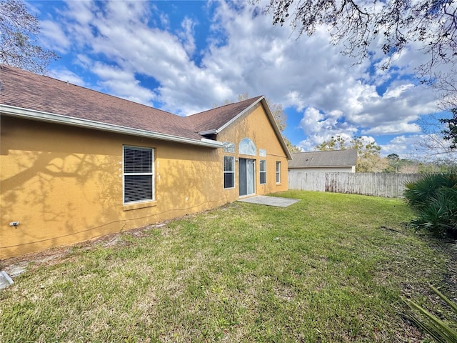 rear view of property with a yard, roof with shingles, fence, and stucco siding