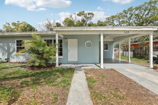 view of front of house with an attached carport, concrete block siding, fence, and driveway