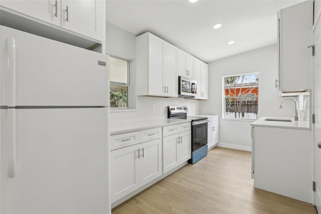 kitchen with a sink, white cabinetry, light countertops, appliances with stainless steel finishes, and light wood finished floors