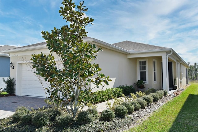 view of home's exterior featuring decorative driveway, a garage, roof with shingles, and stucco siding