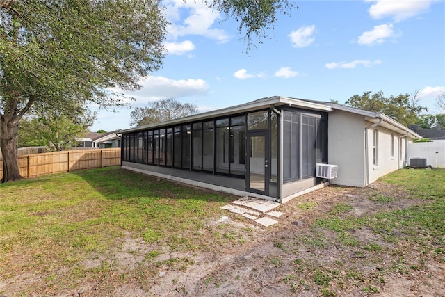 rear view of property featuring a fenced backyard, central AC, a sunroom, a lawn, and stucco siding