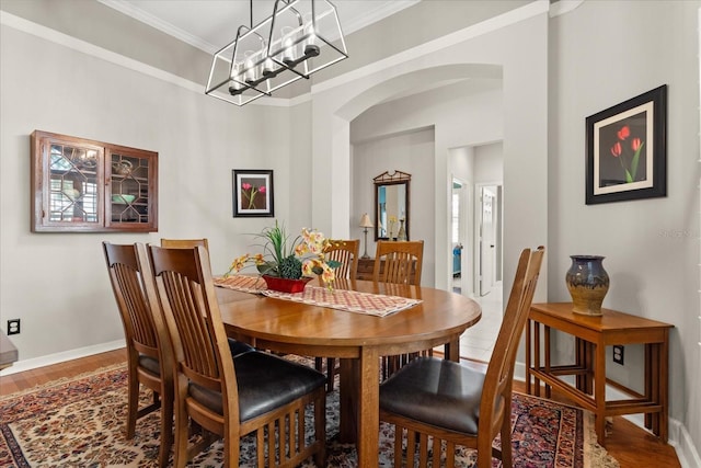 dining room with ornamental molding, arched walkways, baseboards, and wood finished floors