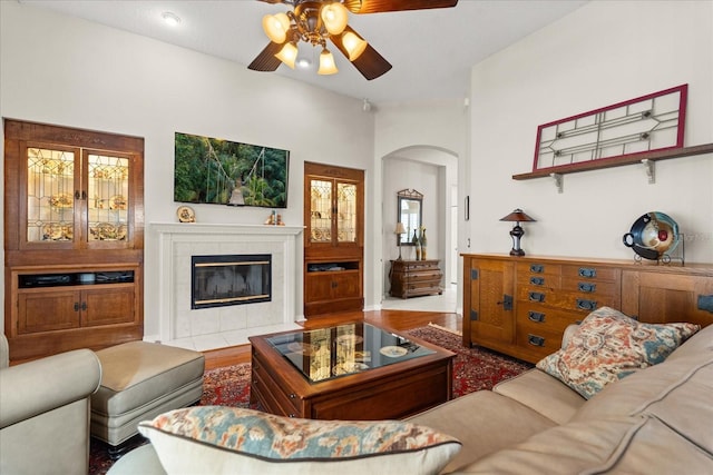 living room with arched walkways, a fireplace, wood finished floors, and a ceiling fan