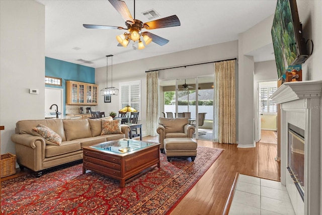 living area with visible vents, baseboards, a glass covered fireplace, ceiling fan, and light wood-style floors