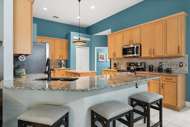 kitchen featuring a breakfast bar, light tile patterned floors, appliances with stainless steel finishes, a sink, and a peninsula