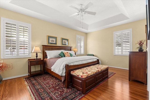 bedroom featuring a tray ceiling, wood finished floors, a ceiling fan, and baseboards